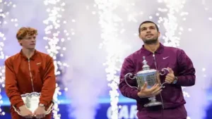 Carlos Alcaraz holds the championship trophy as Jannik Sinner looks
