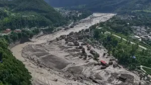 Damaged houses stand precariously near the swollen, debris-choked banks of the Trishuli River